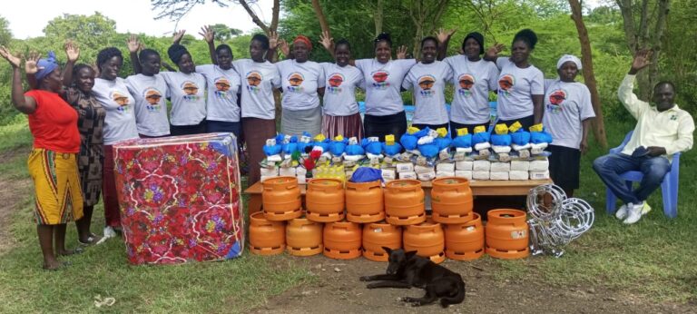 A group of smiling Kenyan Mothers of the Forest (and one man) with gas stoves, rice, oil and sugar as Christmas gifts in 2024