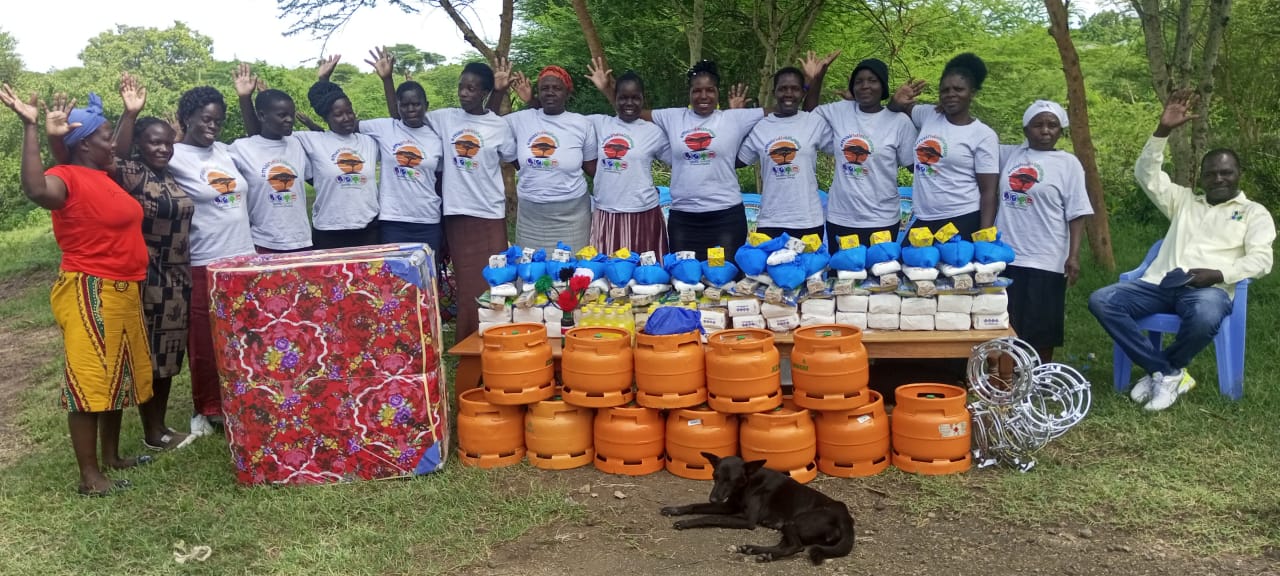 A group of smiling Kenyan Mothers of the Forest (and one man) with gas stoves, rice, oil and sugar as Christmas gifts in 2024