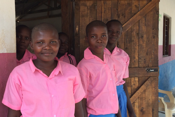 A small group of Kenyan children in pink and blue uniform emerging from a classroom painted white, pink and blue