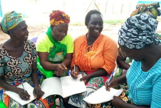 Five smiling Kenyan women writing in exercise books